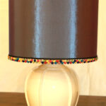 Lampada da tavolo in ceramica con decoto a rilievo e paralume con pon-pon